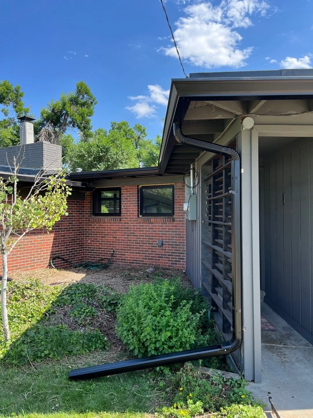 New gutter installation added along the side roofline of a brick home with a flat roof and mature landscaping.