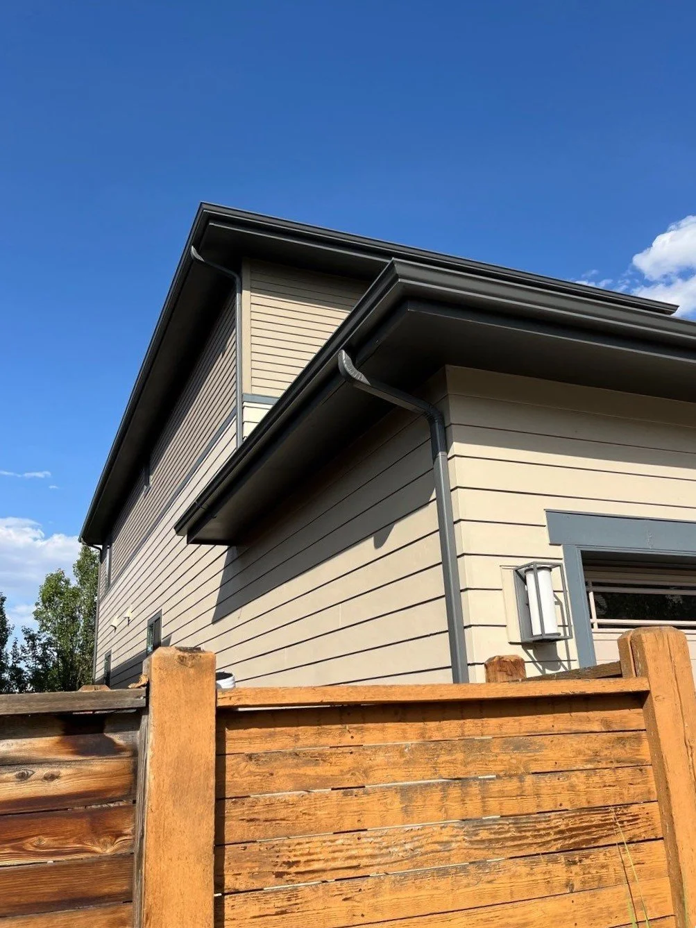 Seamless gutter and downspout installed along the roofline of a siding home.