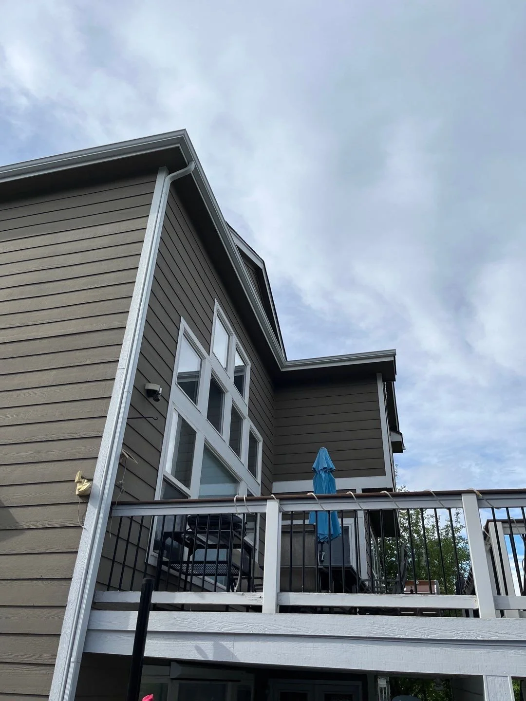 Professional seamless gutter installation fitted to the upper corner of a multi-story siding home.