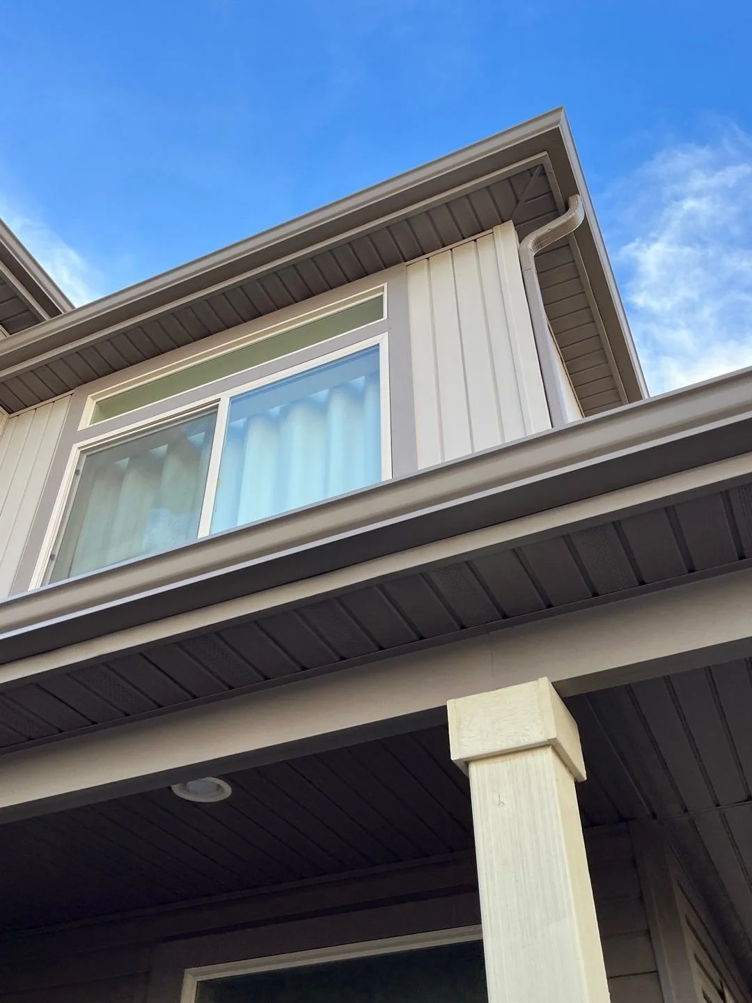 Close-up of a seamless gutter and downspout system beneath an upper-story window.