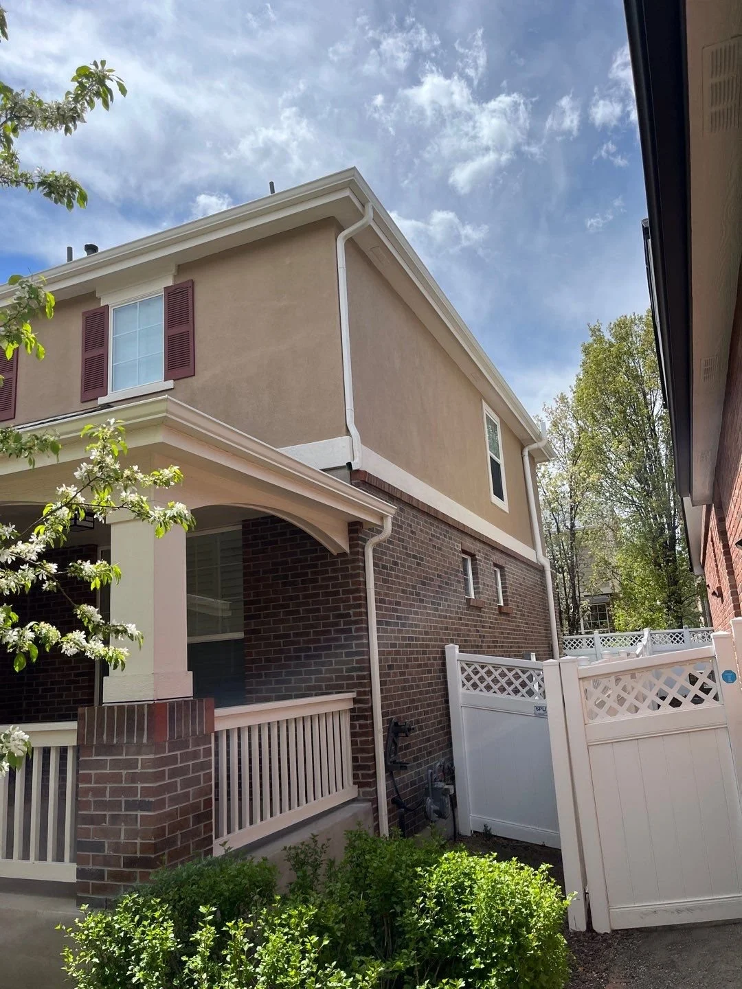Seamless gutters and downspouts installed on a two-story home beside a narrow driveway.