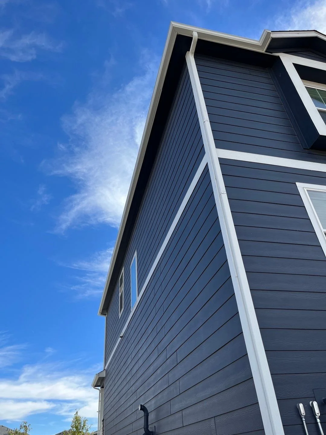 Close-up of white seamless gutters and downspouts installed along the roofline of a blue-sided home.
