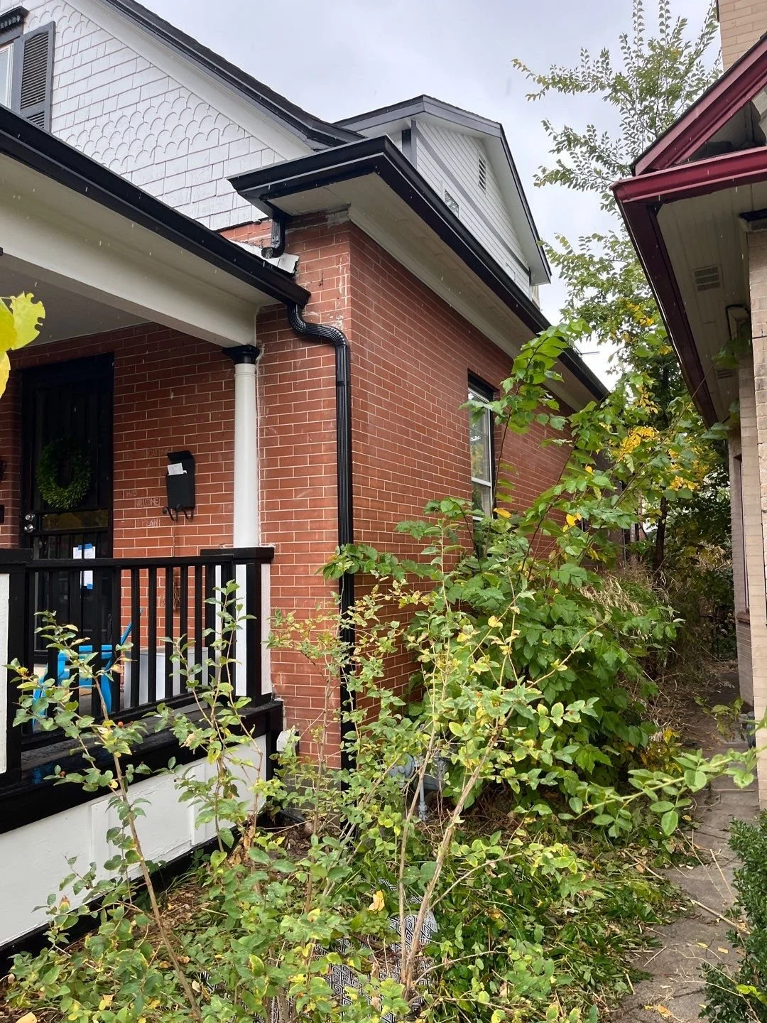 Gutter and downspout installed beside the front porch of a brick home.
