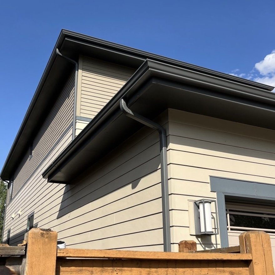 New seamless gutters and downspouts installed along the upper roofline of a siding home.