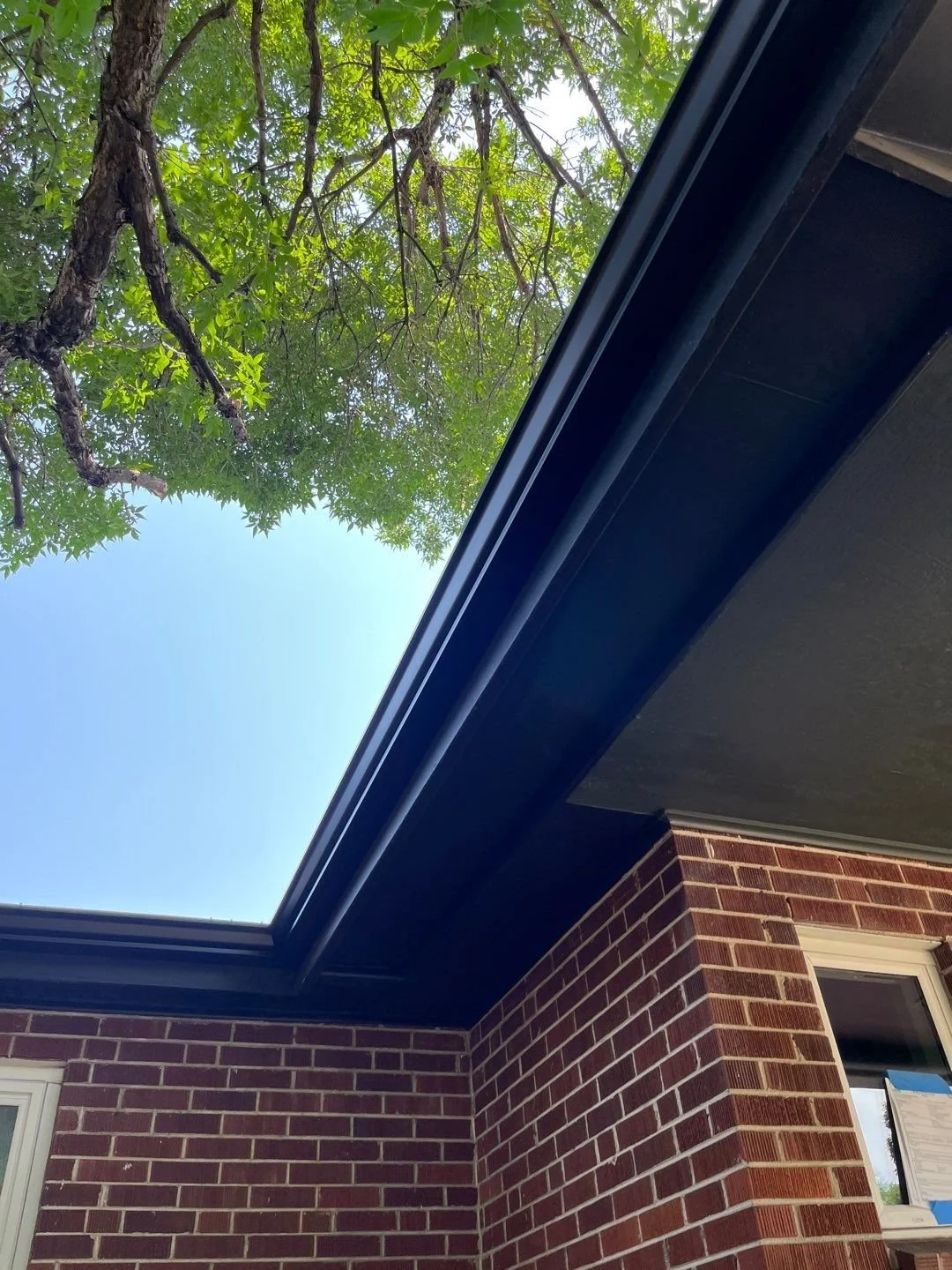 Close-up of a dark seamless gutter installed above a brick exterior wall.