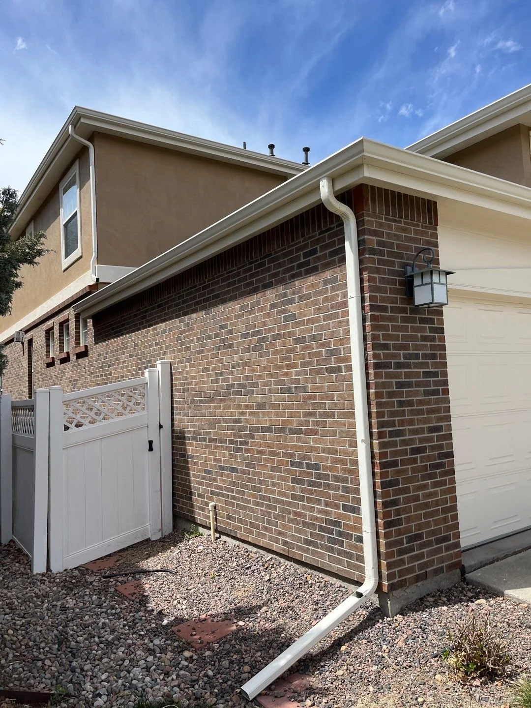 Seamless gutters and downspouts installed along the side of a brick garage.