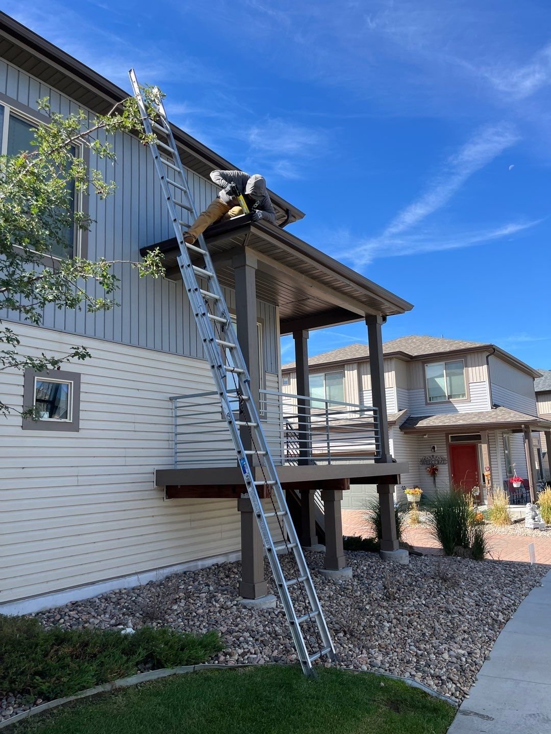 Kelly Gutter installer working from a ladder on the upper roofline of a multi-story home.