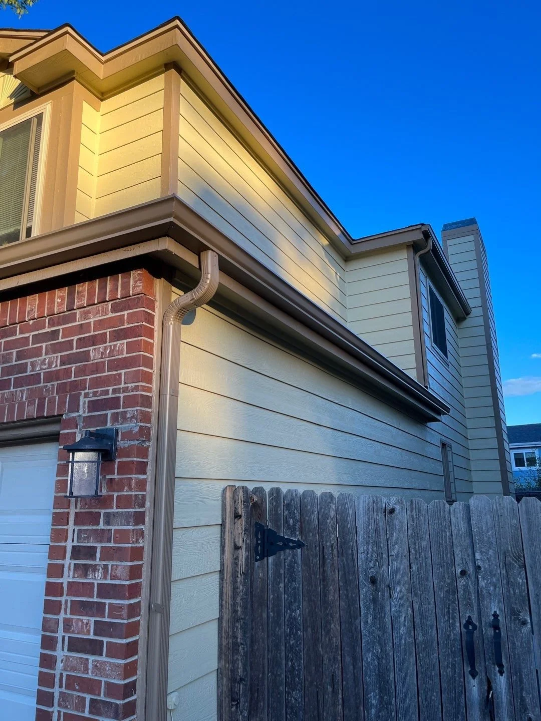 Close-up of cocoa brown seamless gutters and a downspout installed on a brick garage.