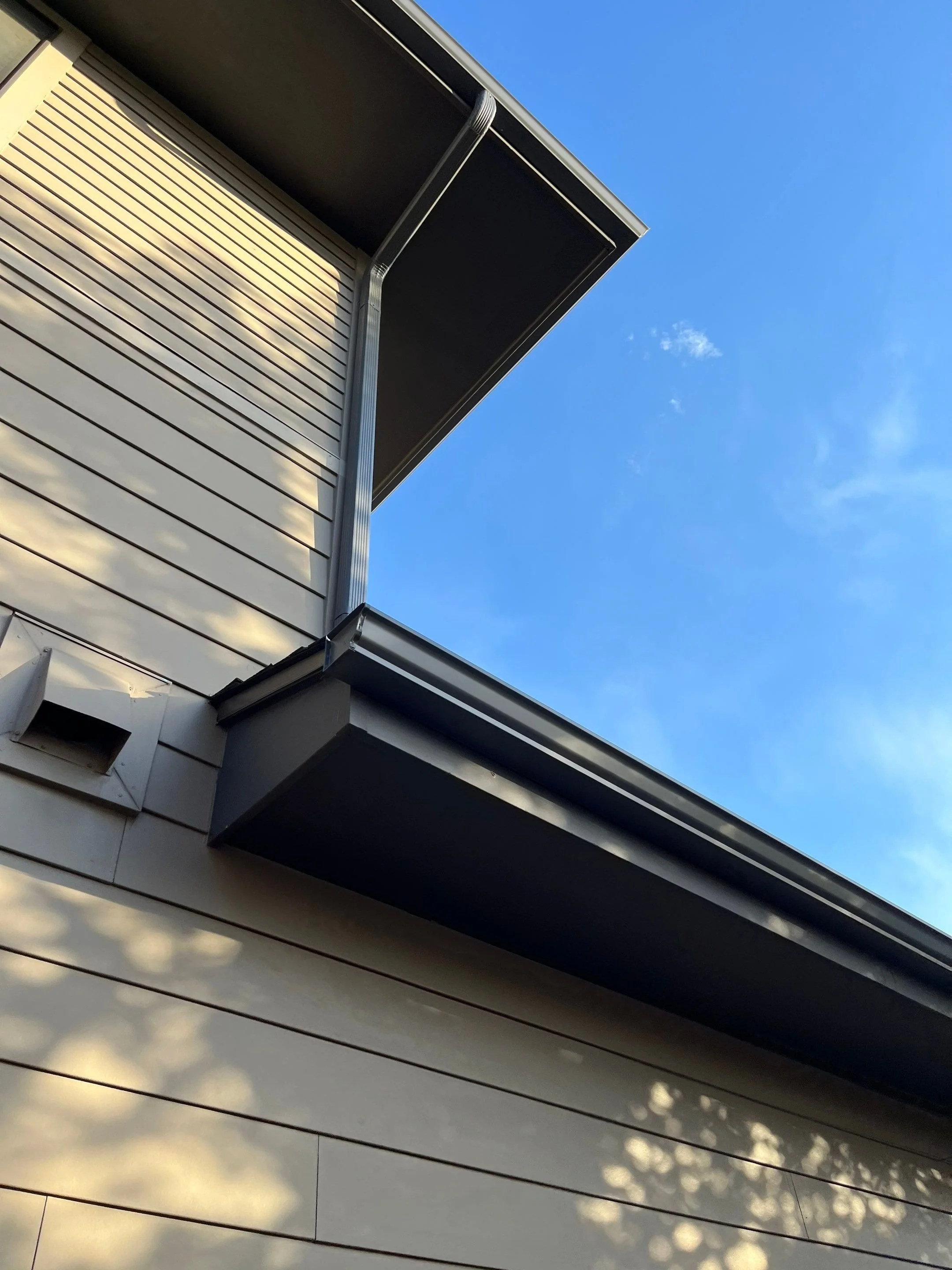 Close-up of a dark gray seamless gutter and corner detail on a siding home.