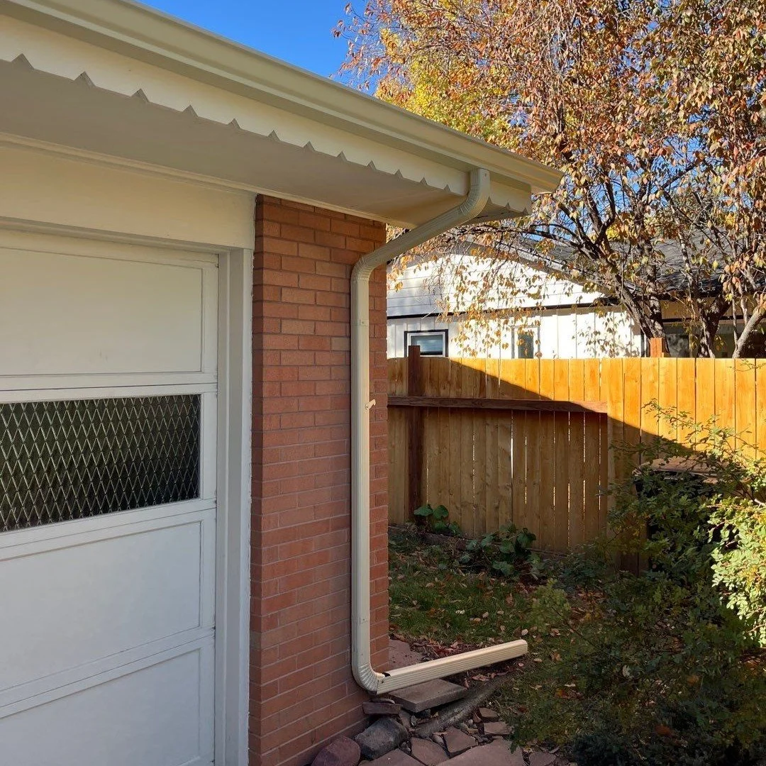 Beige seamless gutter and downspout installed along the garage roofline of a brick home.
