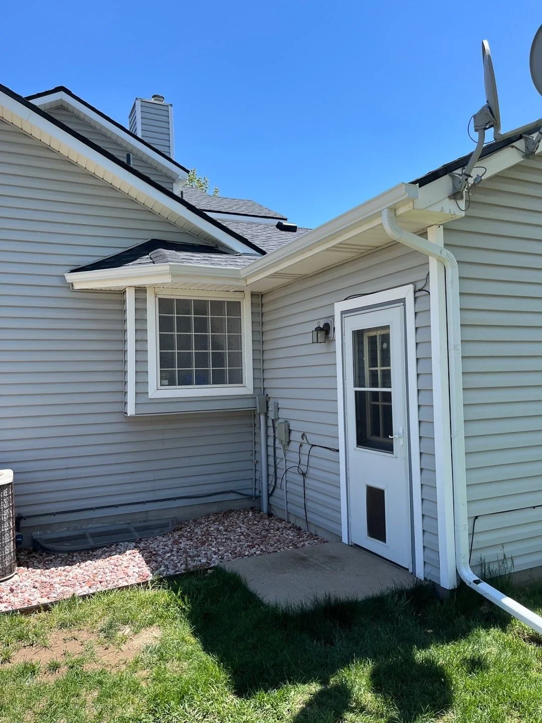 White seamless gutter and downspout installed above a side entry door and bay window.