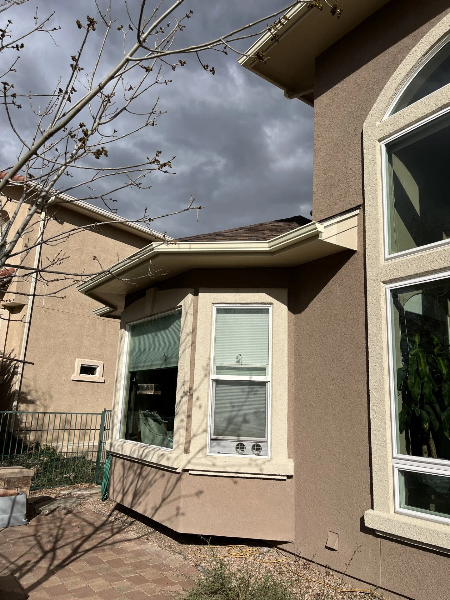 Custom seamless gutter installed above a projecting bay window on a stucco home.