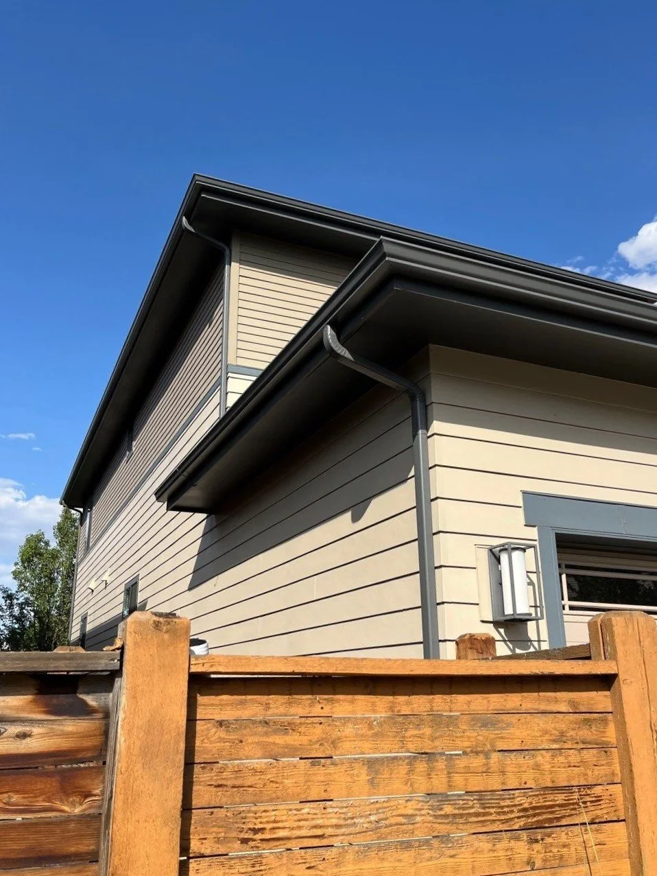 Close-up of a seamless gutter and downspout system above a fenced side yard.