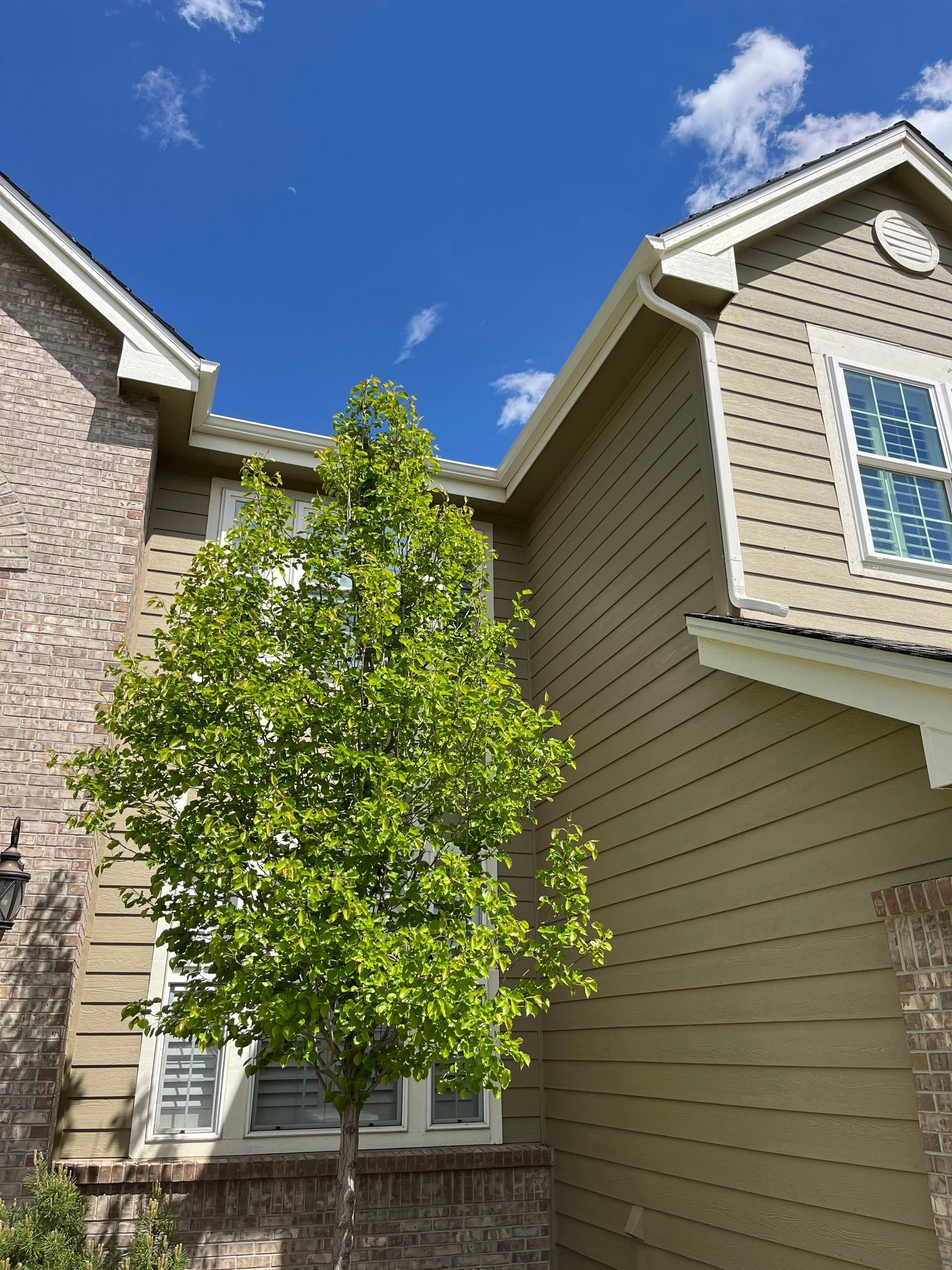 New gutter and downspout system installed along the upper corner of a stone-and-siding home.