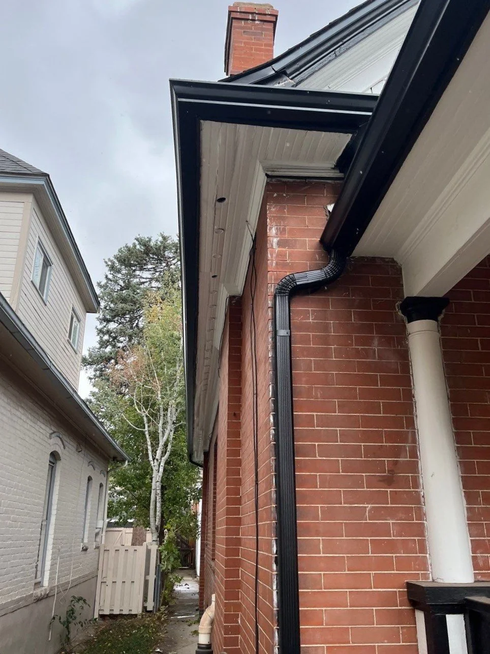 Downspout installed along the brick exterior between two homes.