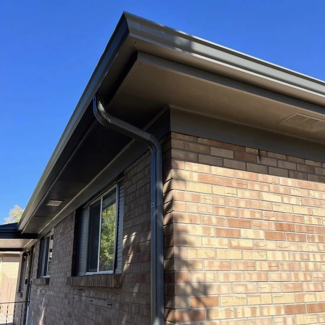 Dark bronze seamless gutter and downspout installed along the roofline of a brick home.