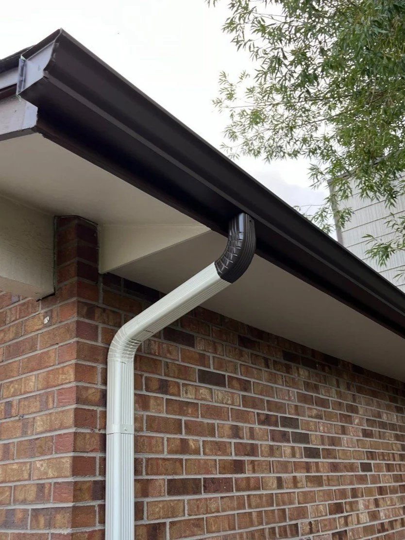 Close-up of seamless gutter replacement with a downspout secured along the brick exterior.