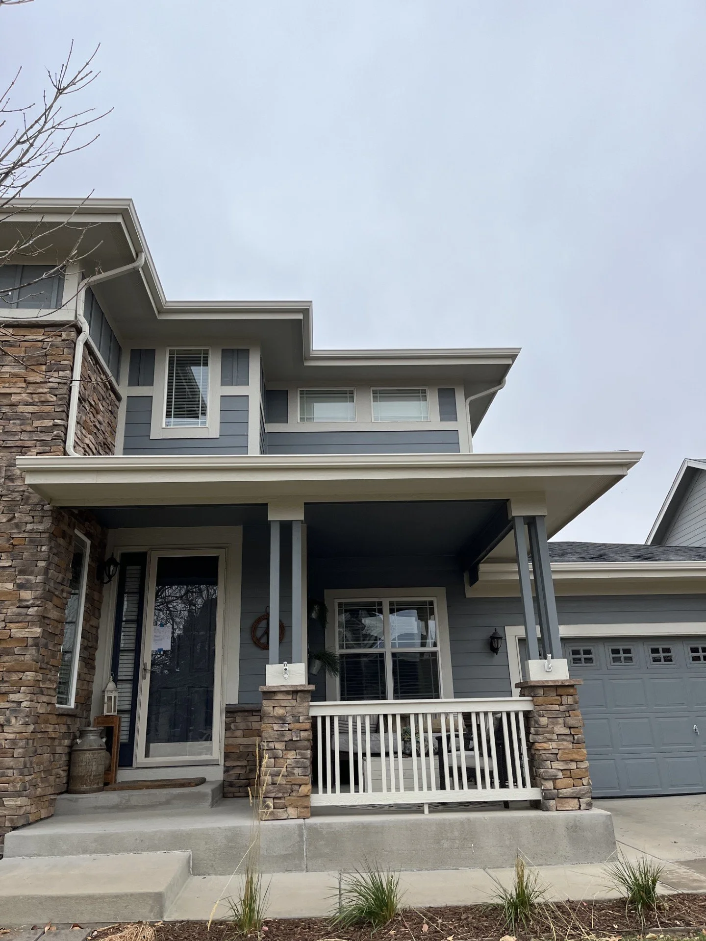 Two-story home with seamless gutters and downspouts installed around the covered front porch.