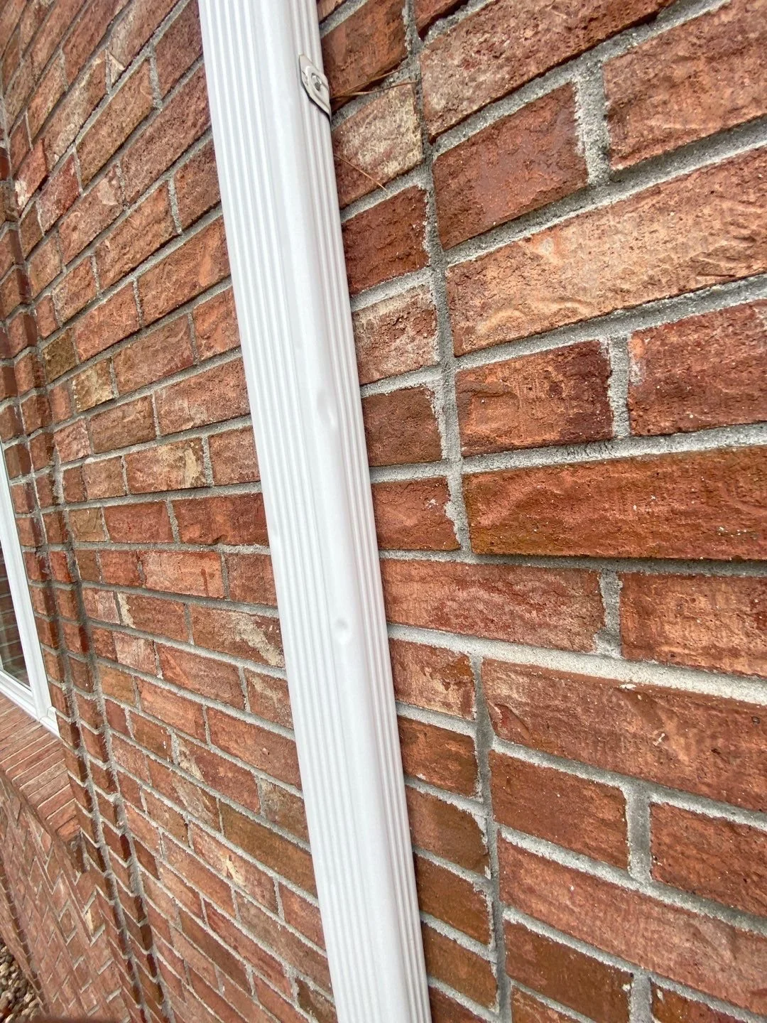 Close-up of hail dents near the bottom of the home’s original gutter downspout before replacement.