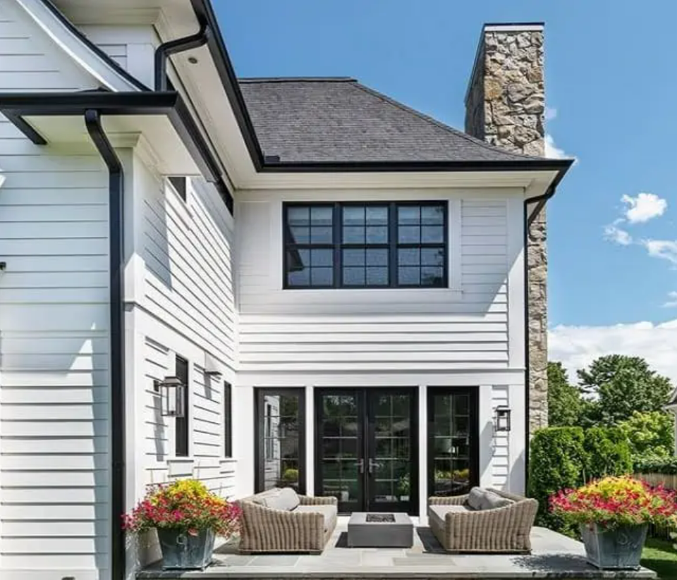 Black seamless gutters and downspouts installed on a home with white siding.