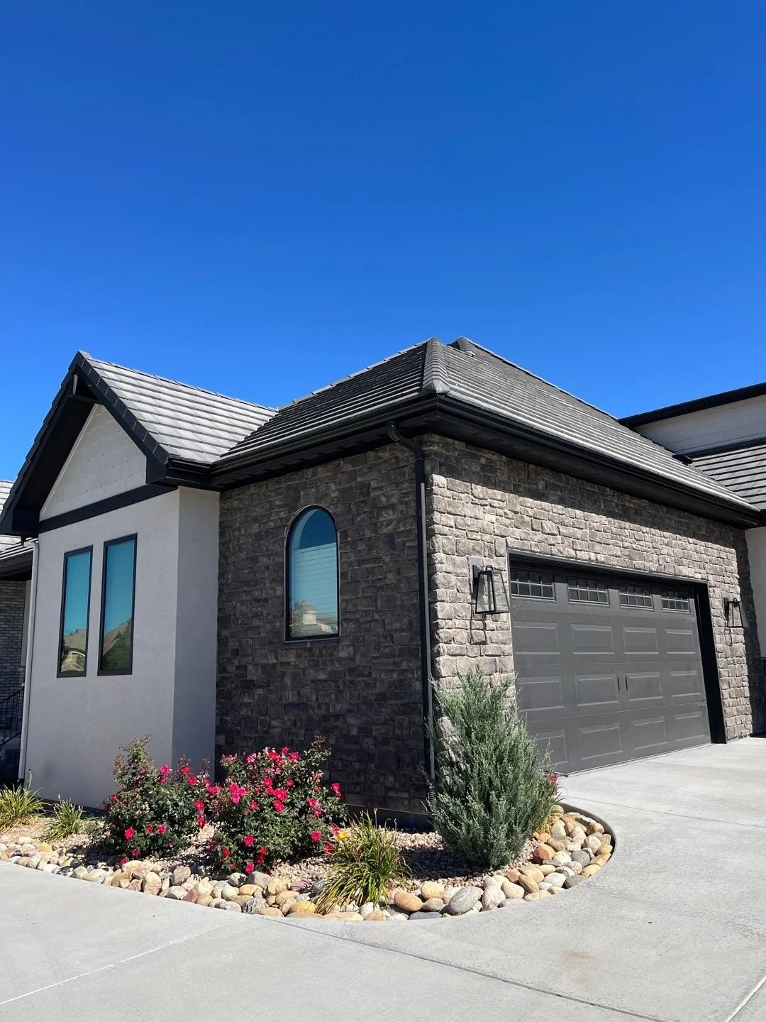 Seamless gutter installation on a stone-front home with landscaped flower beds.