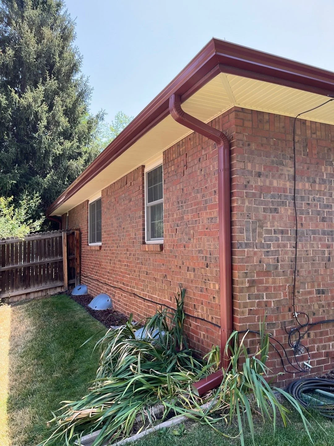 Brick home with redwood seamless gutters and downspouts installed along the side roofline.