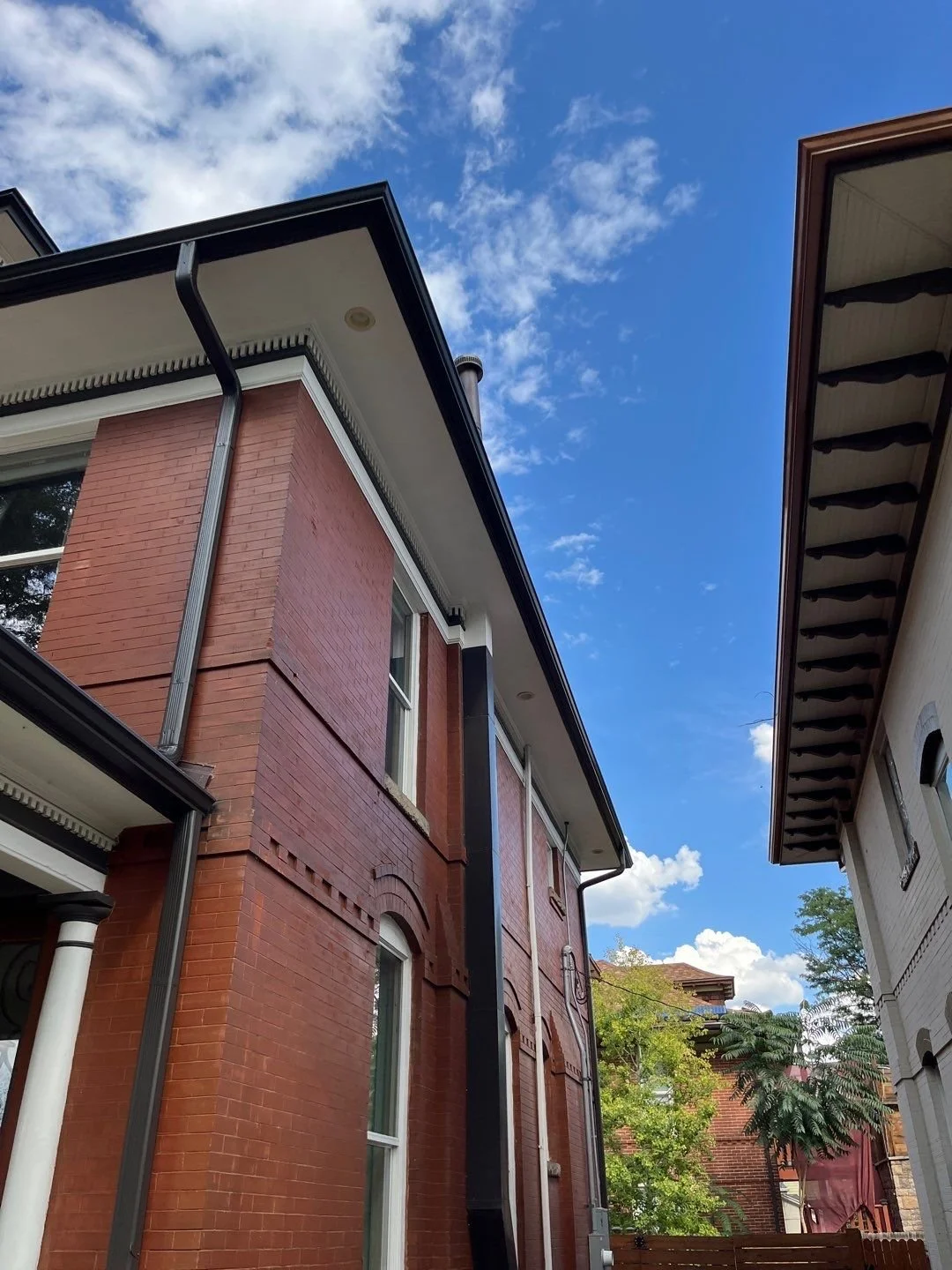 Seamless gutters and downspout installed along the corner of a brick home.