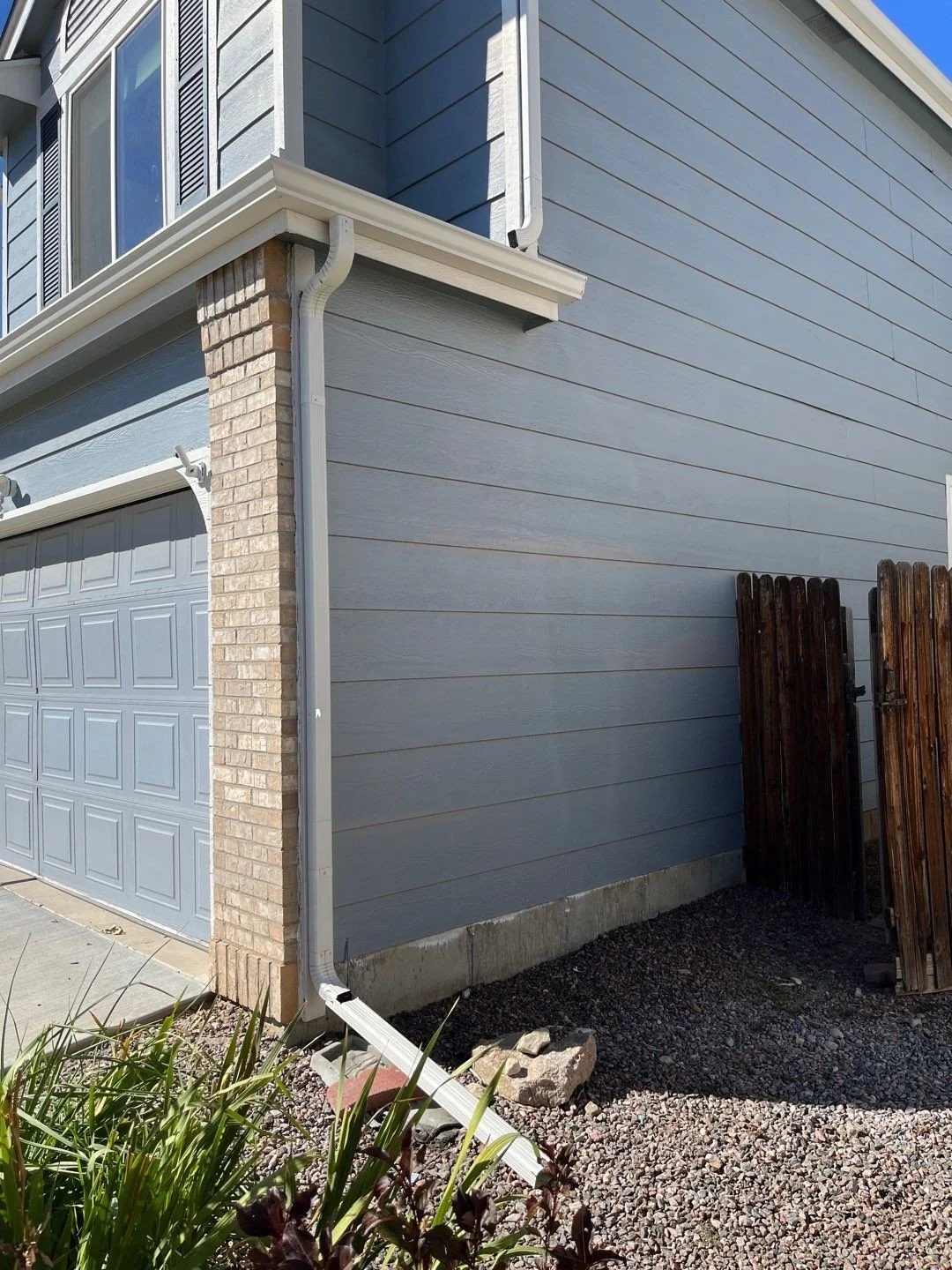 New gutter and downspout replacement installed at the rear corner of a siding home.