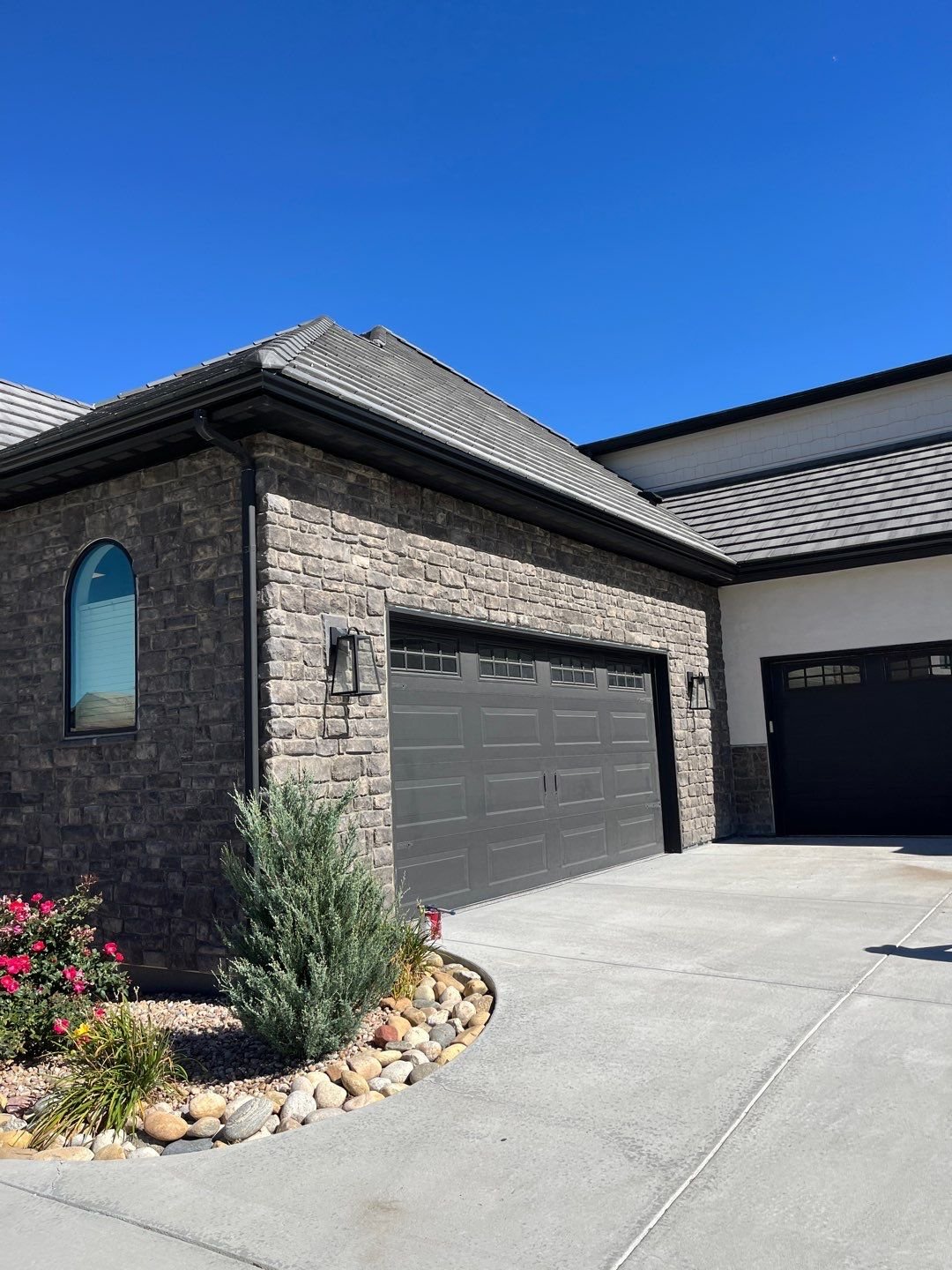 Dark bronze seamless gutters and downspouts installed on a stone-front home with a three-car garage.
