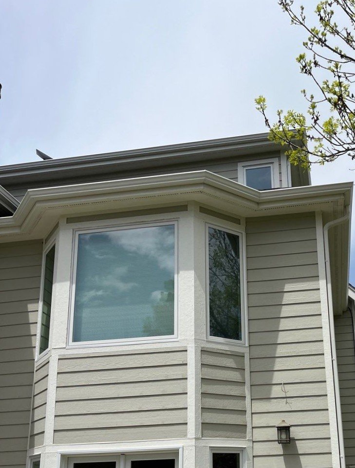 Custom white seamless gutters with hand-cut miters around an upper bay window on a Bayou Hills home.