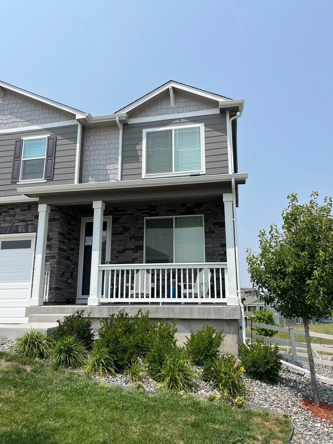 White seamless gutters and downspouts installed on a gray two-story home with a covered front porch.