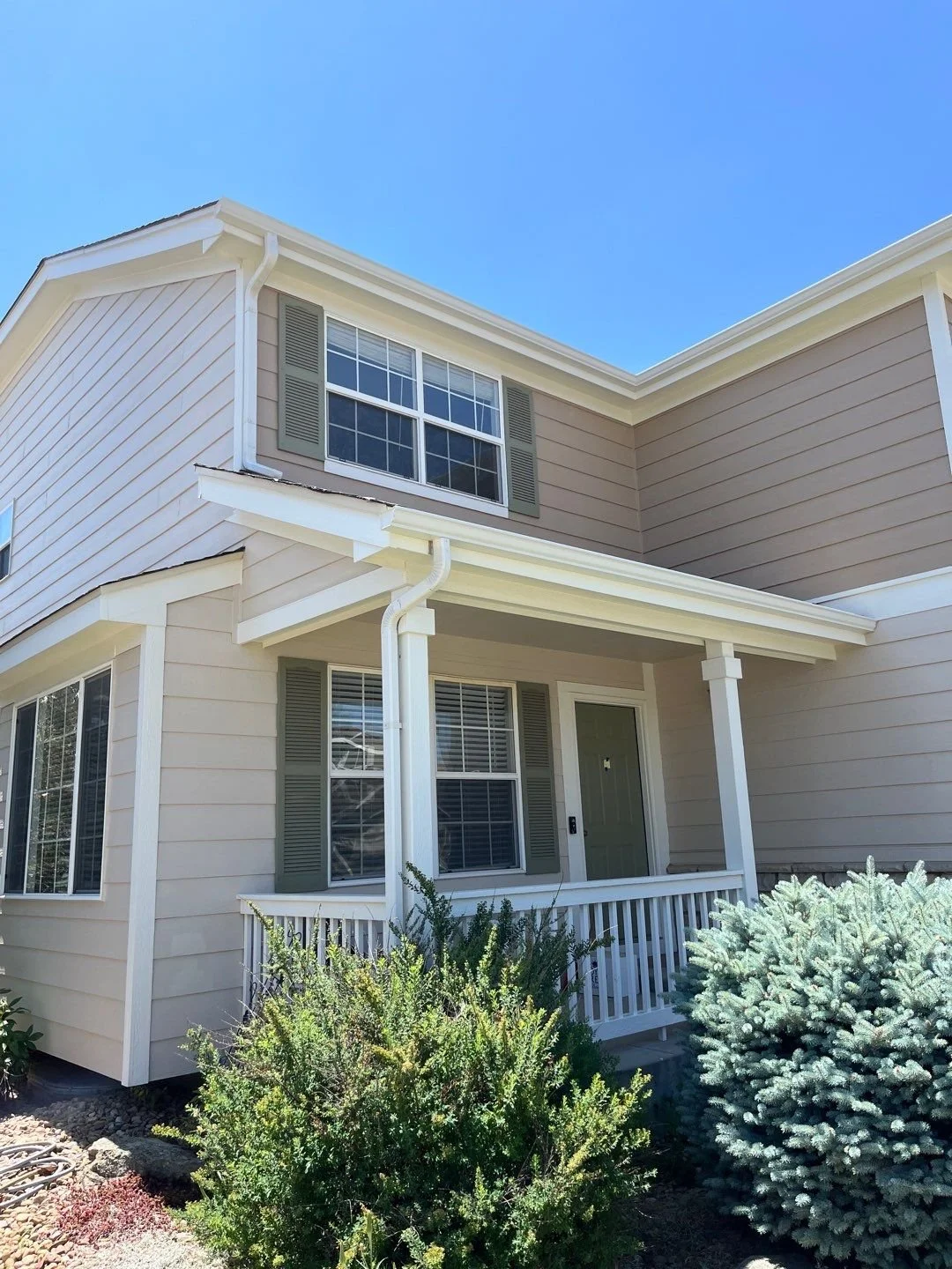 Seamless gutter installation fitted around the front porch and upper roofline of a light-colored two-story home.