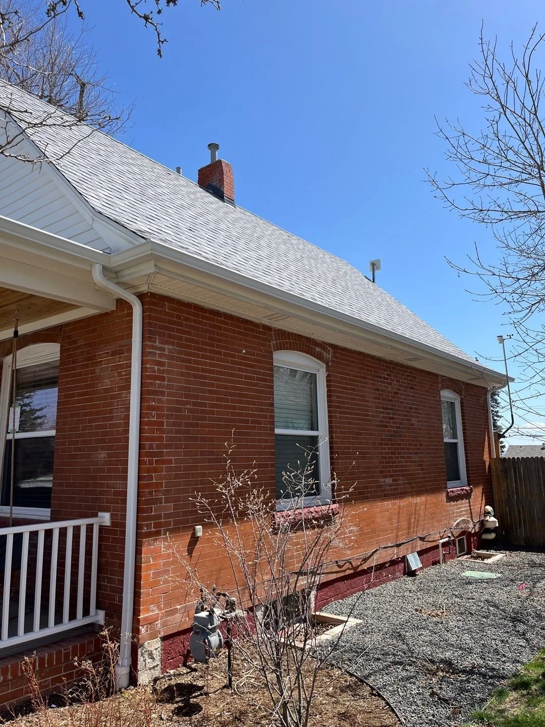 Brick home with seamless gutters and downspouts installed along the side roofline.