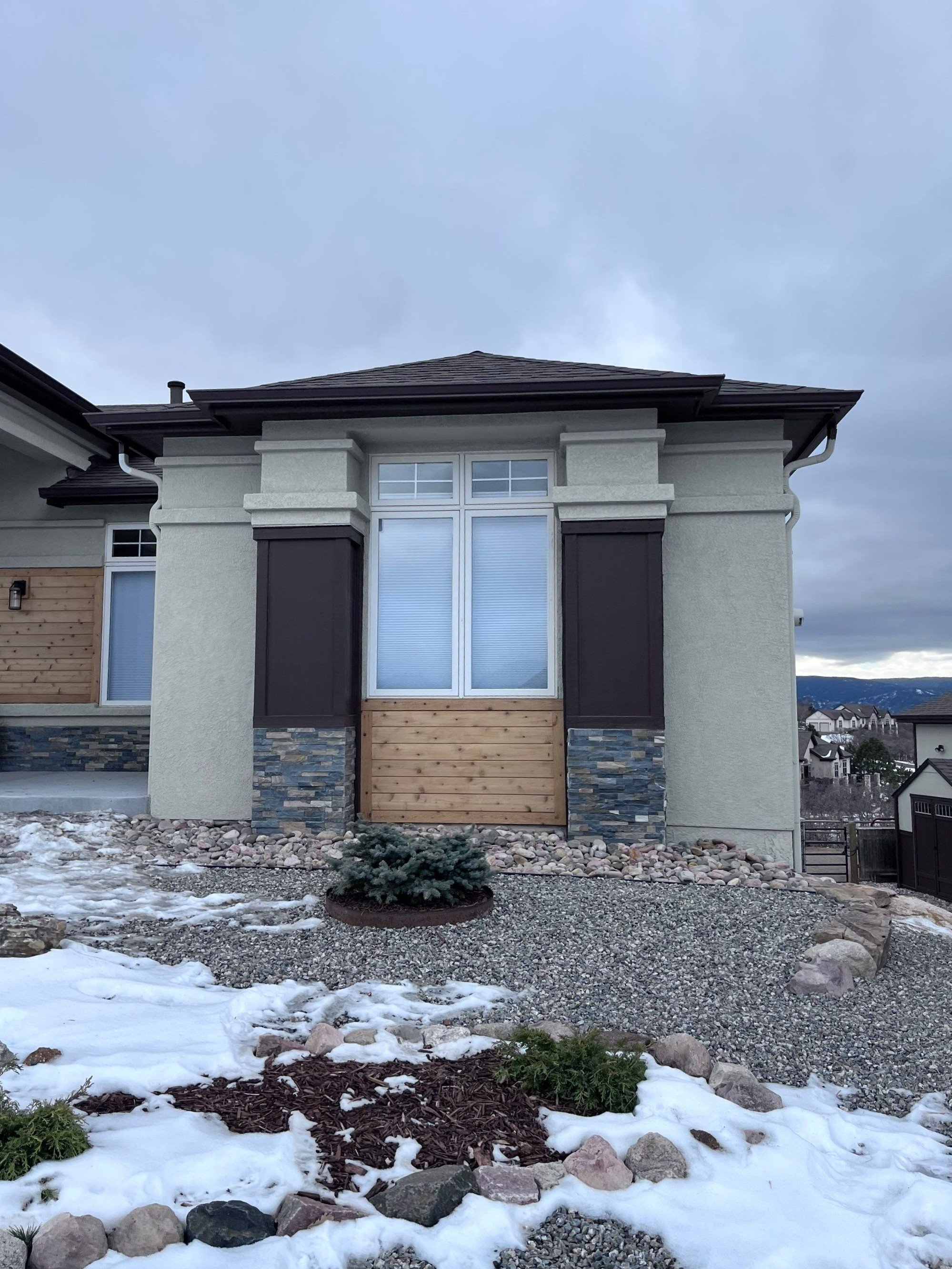 Dark bronze seamless gutters and downspouts installed on a modern gray home with snow around the foundation.