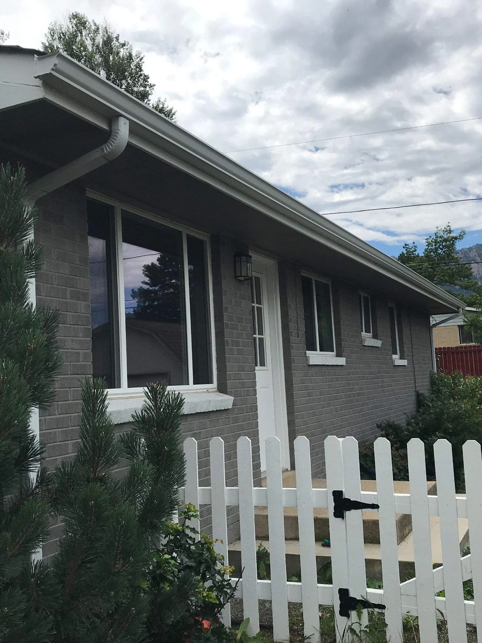 Dark gray home with white seamless gutters and a downspout beside the front windows.