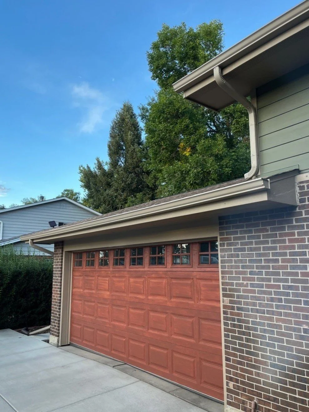 New seamless gutters and downspouts installed above a brick garage with a custom roof transition.
