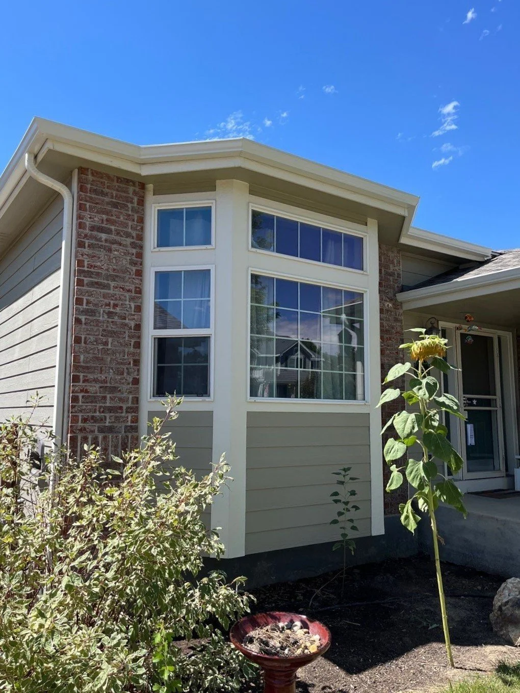 A custom seamless gutter system wraps the projecting bay window section and blends with the home’s mixed exterior materials.