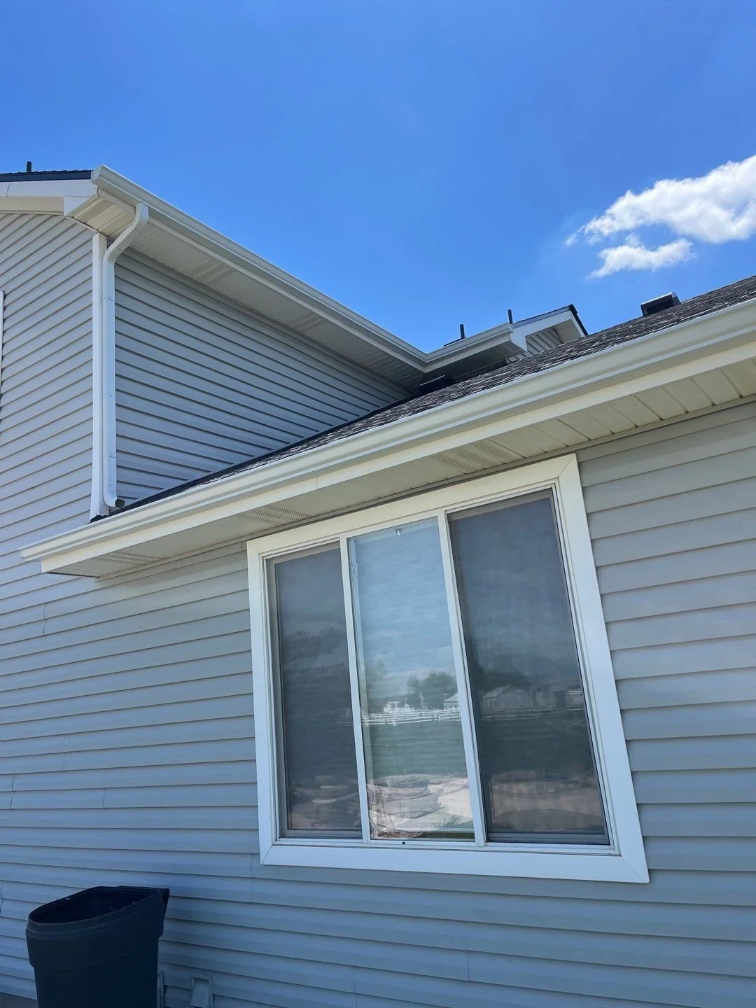 White seamless gutter installed above a window on a blue-sided home.