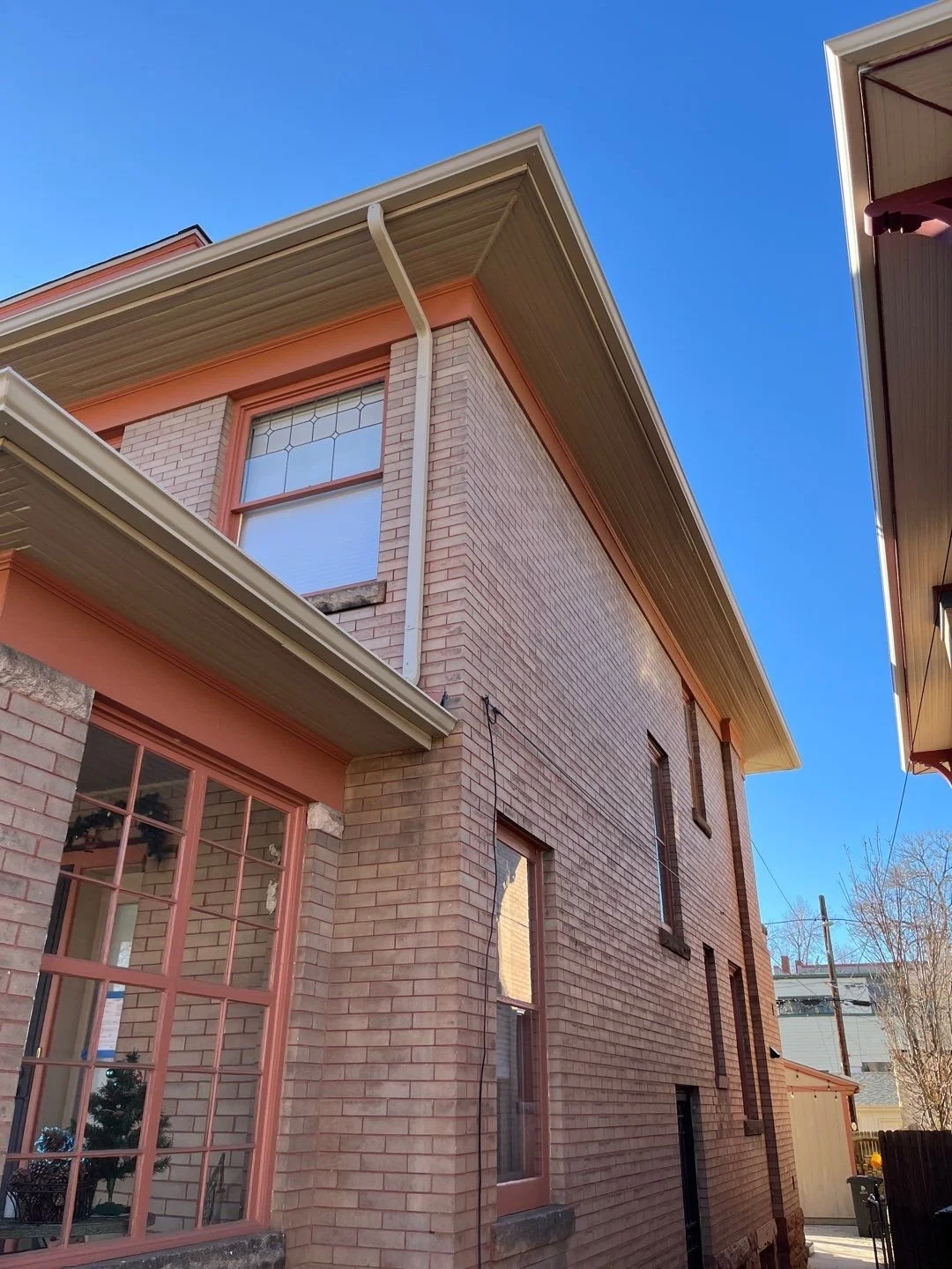 Seamless gutters and downspouts installed along the upper roofline of a brick home.