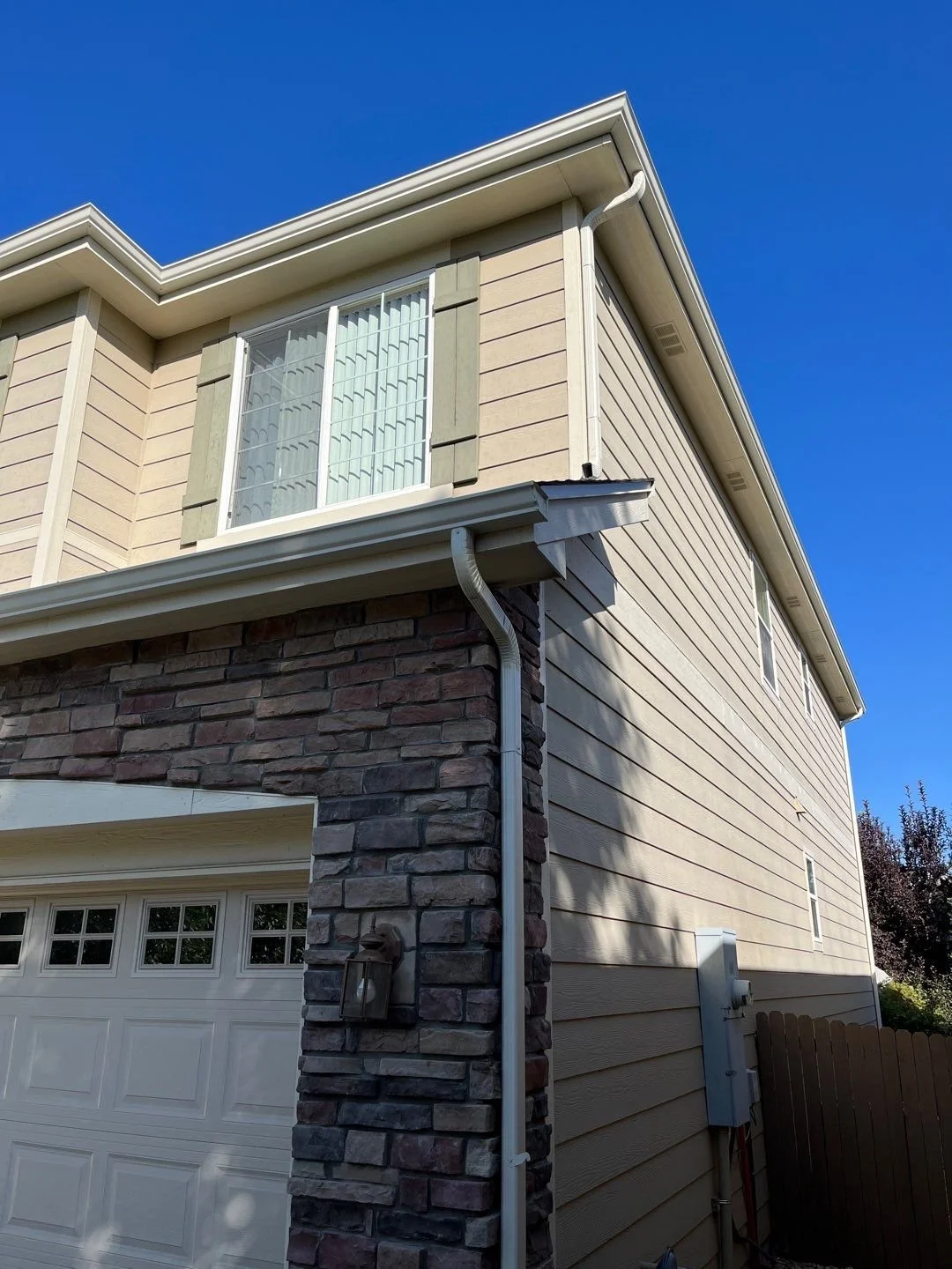 Custom gutters and downspouts follow the stone-and-siding corner of this two-story home.