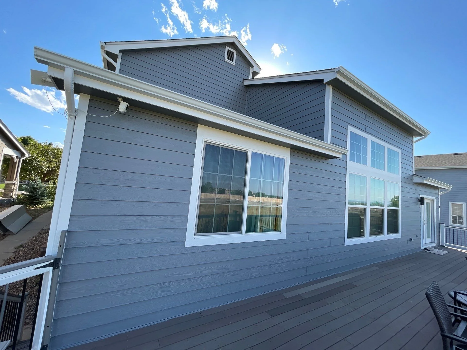 New white seamless gutters and downspouts installed along the side of a light-blue residential home.