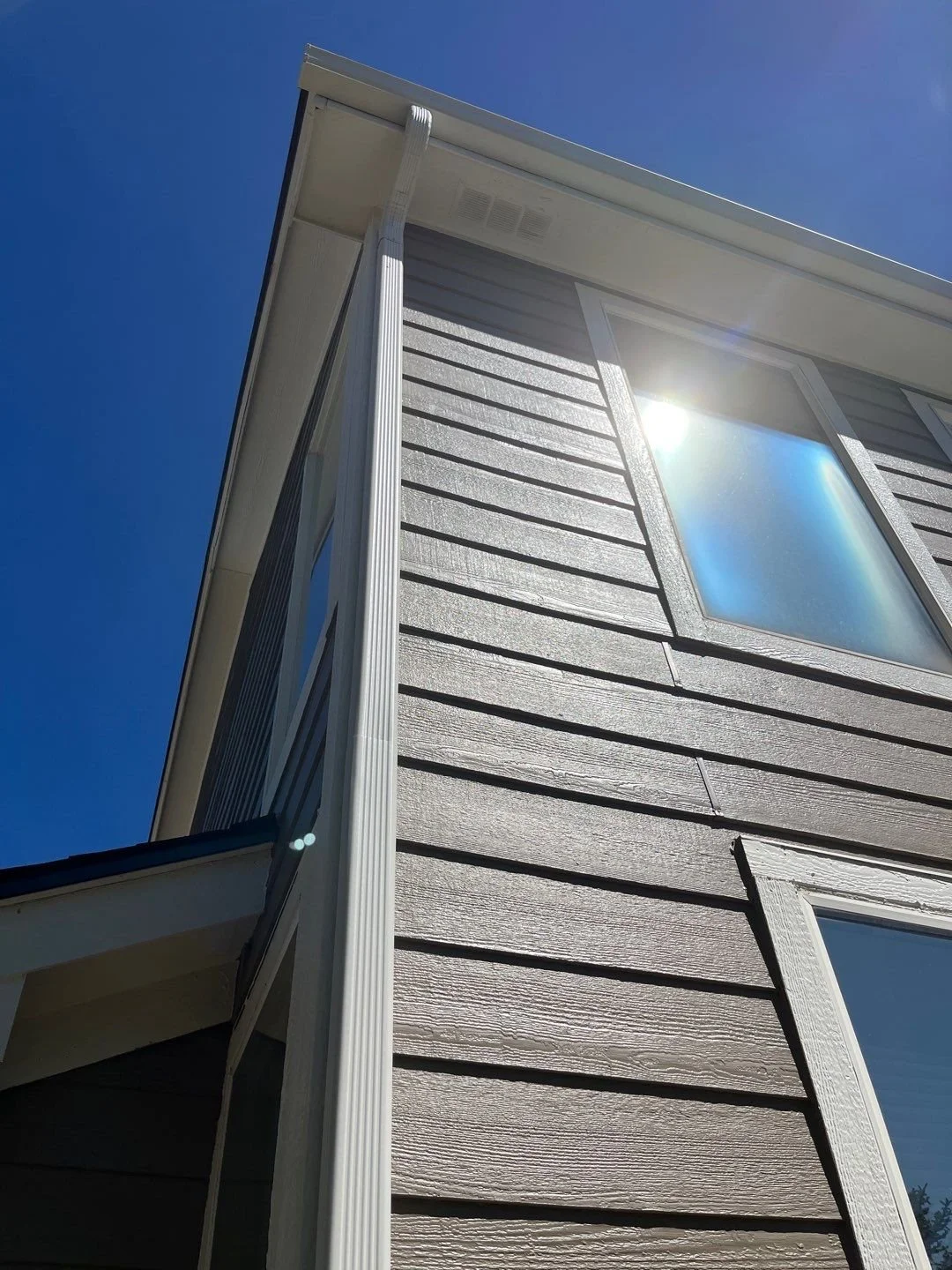 Close-up of a new seamless gutter and downspout system installed along the upper corner of a siding home.