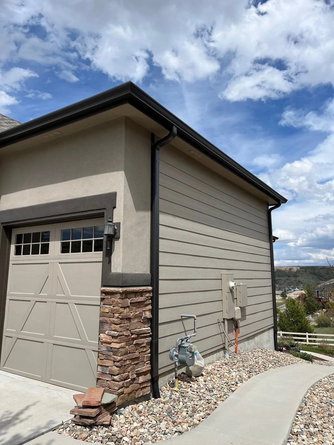 Royal Brown seamless gutter and downspout installed along the corner of a sand colored home.