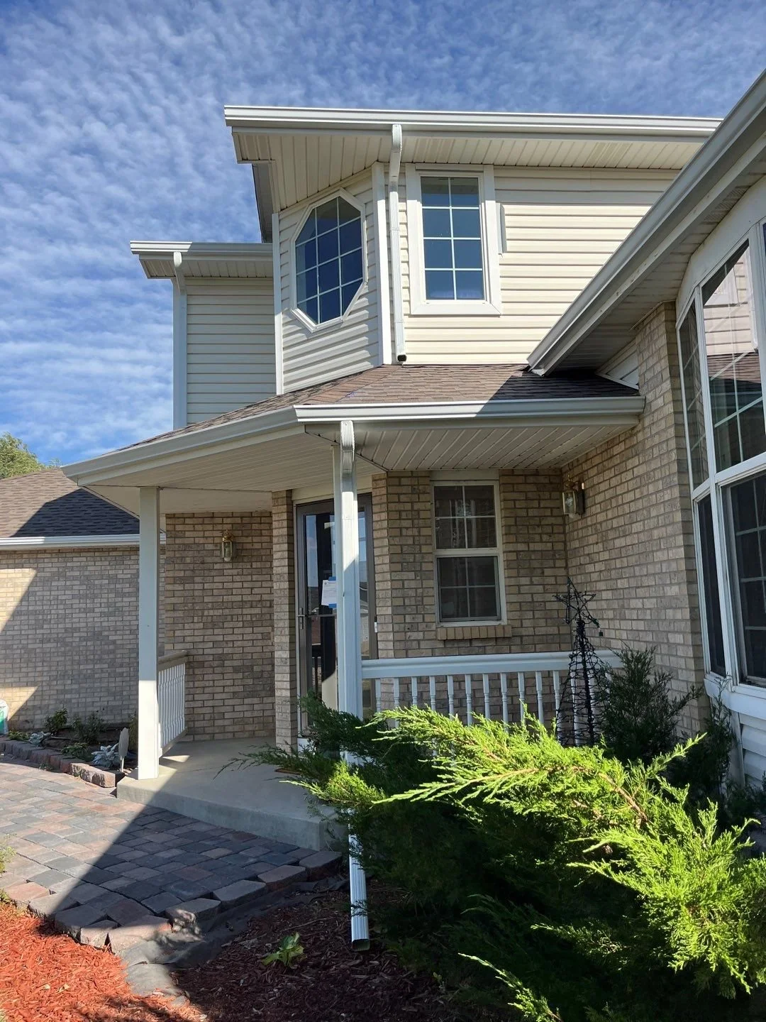 Front entry of a brick-and-siding home with white seamless gutters and downspouts.