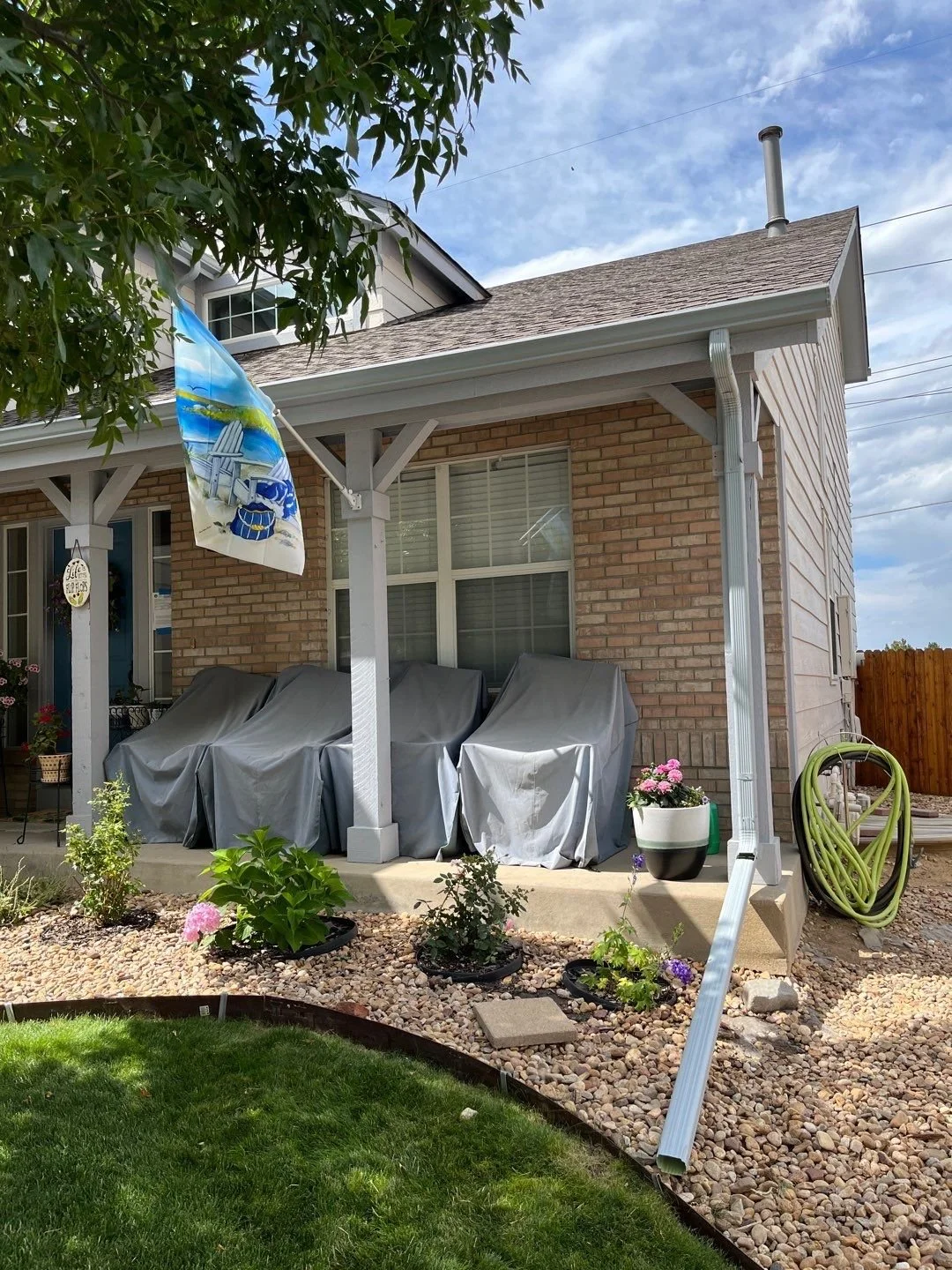 White seamless gutters and downspouts installed around the front porch of a brick home.