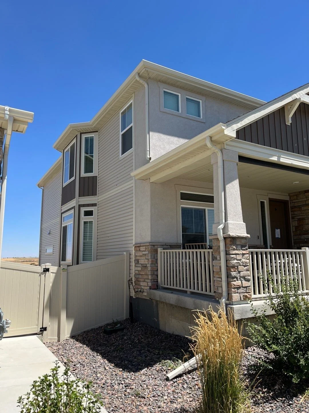 Exterior view of a modern multi-story house with a stone and siding facade, white trim, and a small porch, under a clear blue sky.