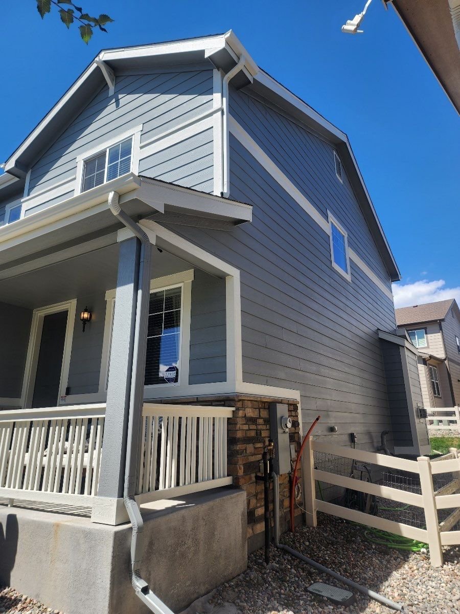 White seamless gutters and downspouts installed along the side of a blue two-story home.