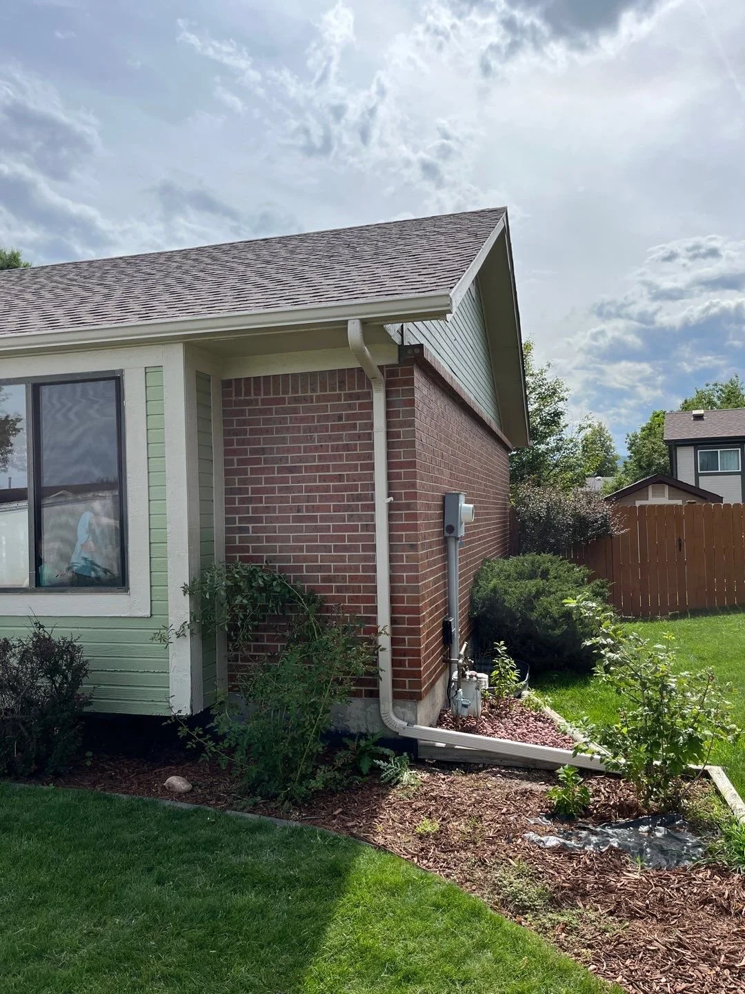 Seamless gutter replacement with new gutters and downspouts installed on a brick-and-siding home.