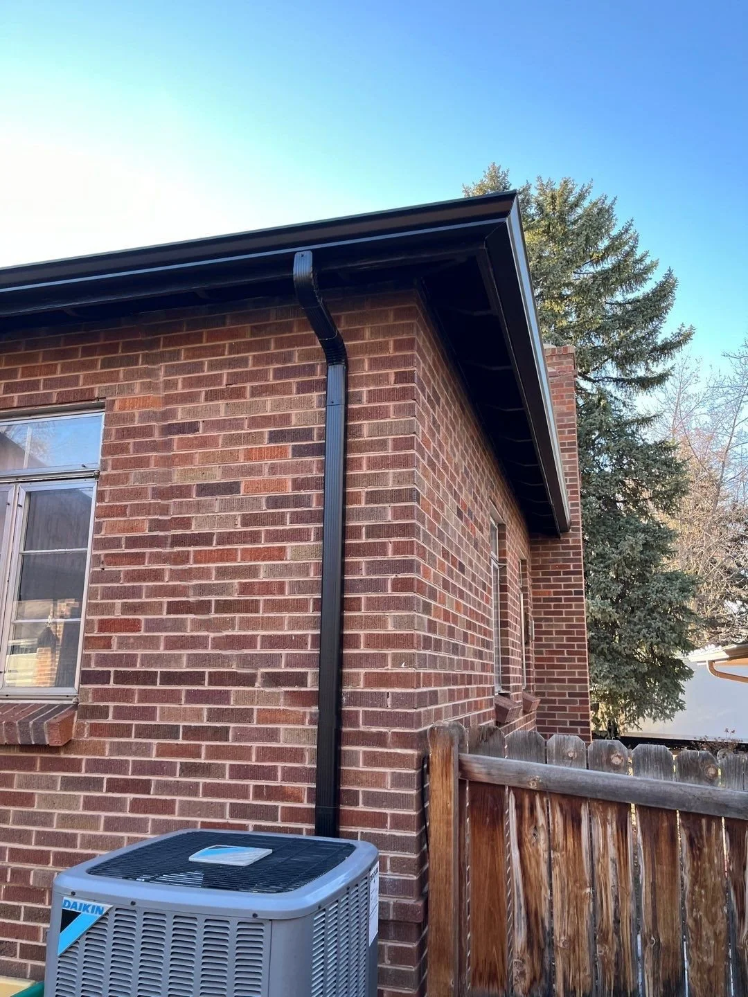 Brick home with seamless gutters and downspouts installed along the rear exterior.