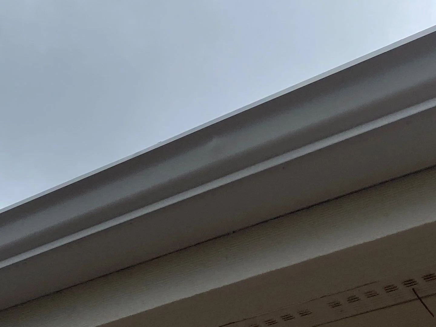 Hail dents along the original aluminum gutter before replacement on a Bayou Hills home.